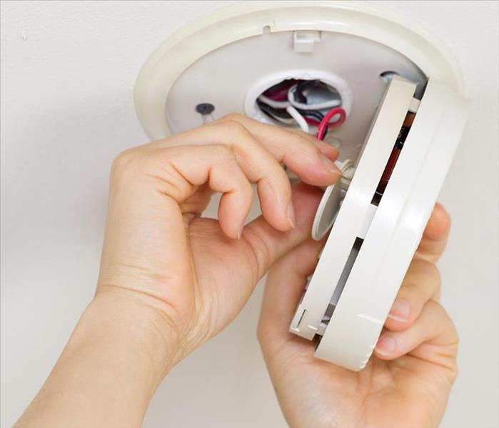 Horizontal photo of female hands taking home smoke detector apart with white ceiling background